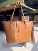 The spacious Caramel Tote Bag, available in a rich brown color, features a secure design with a locking system, a small pouch, and a comfortable leather strap. It offers ample storage space and is available in Pakistan.