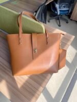 The spacious Caramel Tote Bag, available in a rich brown color, features a secure design with a locking system, a small pouch, and a comfortable leather strap. It offers ample storage space and is available in Pakistan.