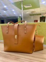 The spacious Caramel Tote Bag, available in a rich brown color, features a secure design with a locking system, a small pouch, and a comfortable leather strap. It offers ample storage space and is available in Pakistan.